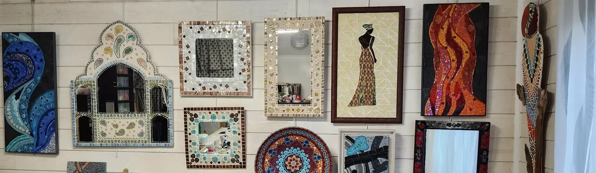 Créations en mosaïque de l'Atelier ARTE MOSAIC exposées sur un mur : miroirs, silhouette et pièces décoratives colorées